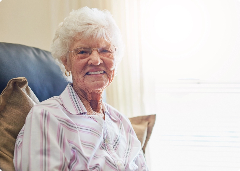 Elderly woman sitting smiling at the camera.