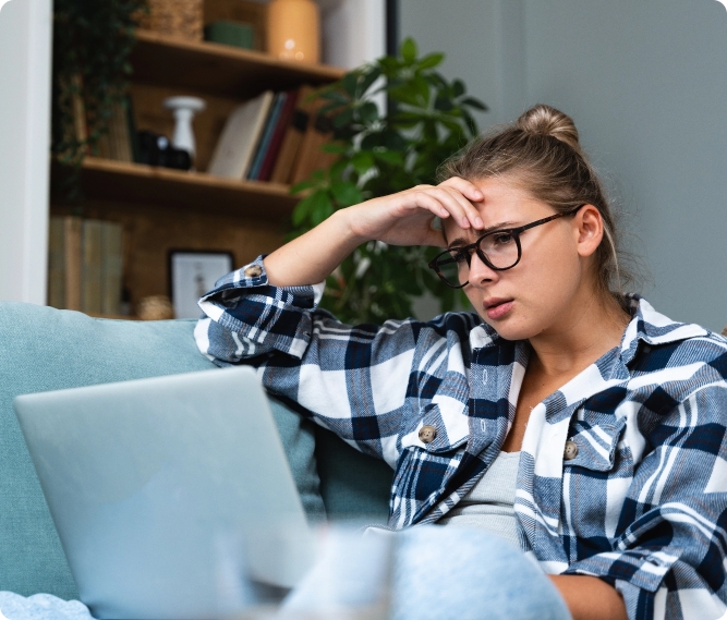 young woman sitting on the sofa looking at her laptop looking distressed